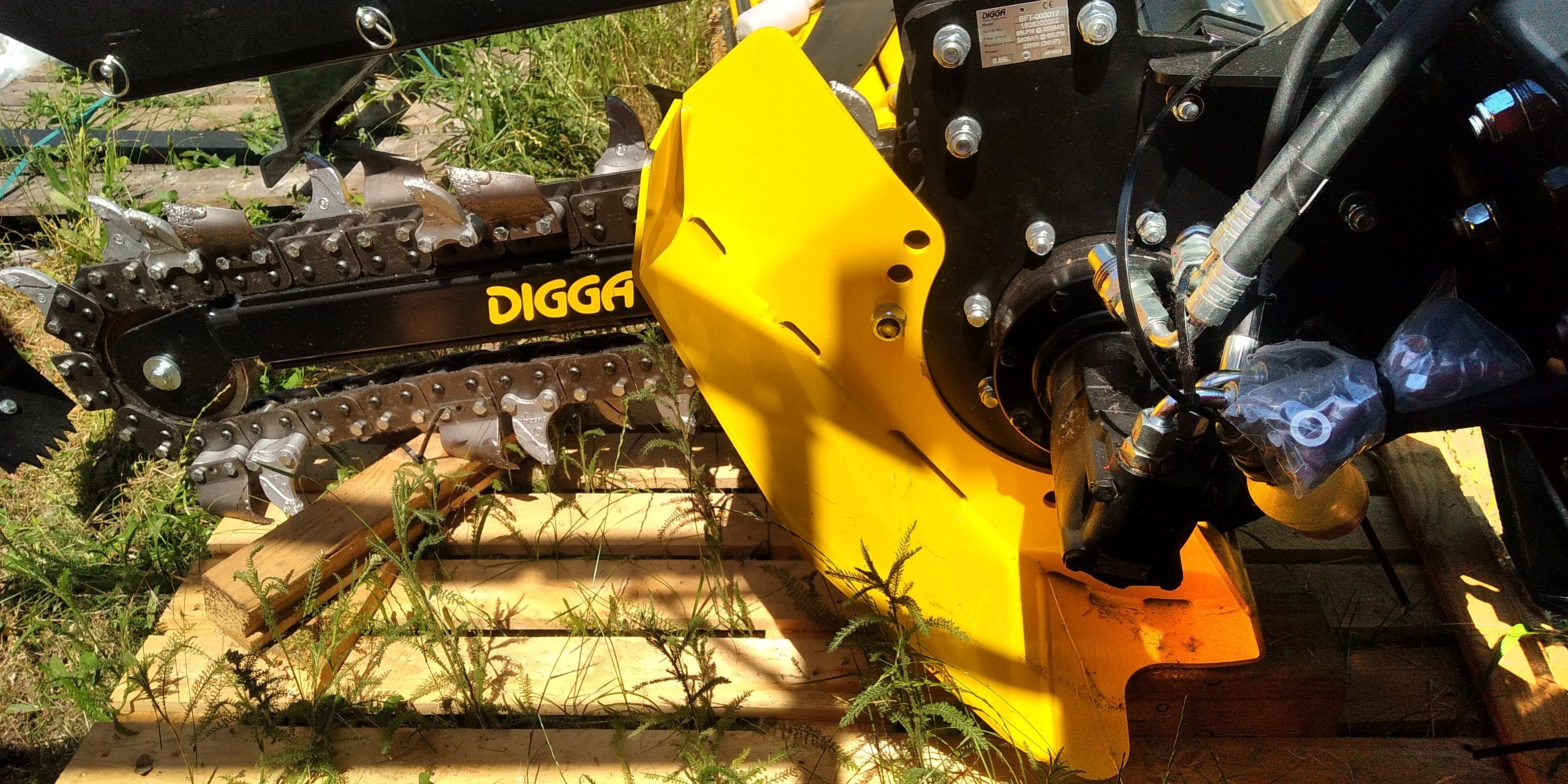 Close-up of a yellow and black Digga trenching machine part resting on a wooden pallet outdoors.